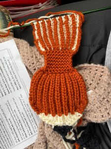 The beginning of a fox head and a short length of the scarf still on a long green double pointed needle